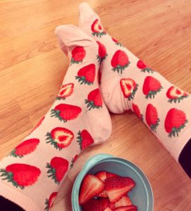 Woman wearing strawberry socks next to a bowl of strawberries