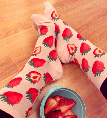 Woman wearing strawberry socks next to a bowl of strawberries