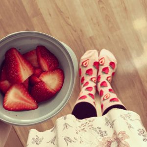 Strawberry socks by ModSocks are worn by a woman holding fresh strawberries.