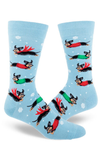 Light blue men's crew socks dotted with small snowflakes feature an allover pattern of leaping black and tan dachshund dogs wearing red and green winter garb.
