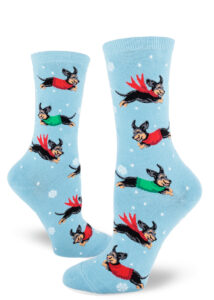 Light blue women's crew socks dotted with small snowflakes feature an allover pattern of leaping black and tan dachshund dogs wearing red and green winter garb.