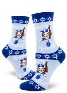 Hanukkah socks that say "Happy Hanukkat" feature a cat spinning the dreidel while wearing a kippah or yarmulke.