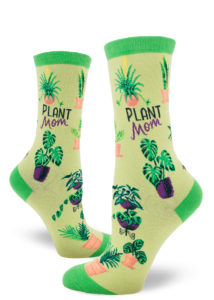 Cute women's crew socks in shades of green say "Plant Mom" on the side with an all-over pattern of various houseplants.