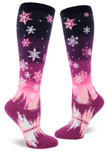 Snowflake knee socks depict a winter scene over a pink and purple gradient striped sky.
